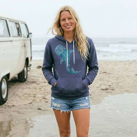 Woman wearing a navy blue hoodie with whale shark design on a beach.