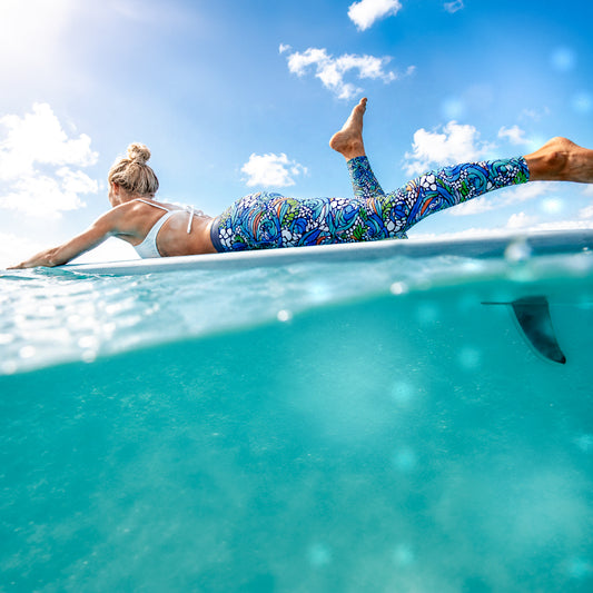 Woman lying on a surfboard wearing octopus ink bore tide leggings