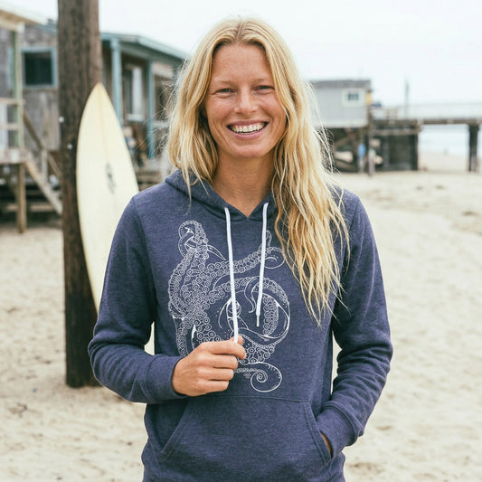 Woman wearing a navy hoodie with a white octopus on a beach